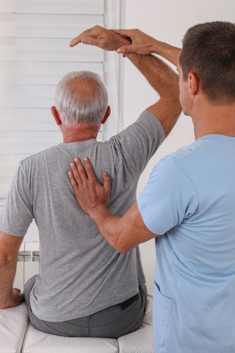 A chiropractic therapist checks the arm flexibility of an elderly man during a rehabilitation session in Manhattan, NY. The man is seated, and the therapist stands behind him, gently guiding his arm. A chiropractic therapist checks the arm flexibility of an elderly man during a rehabilitation session in Manhattan, NY. The man is seated, and the therapist stands behind him, gently guiding his arm.