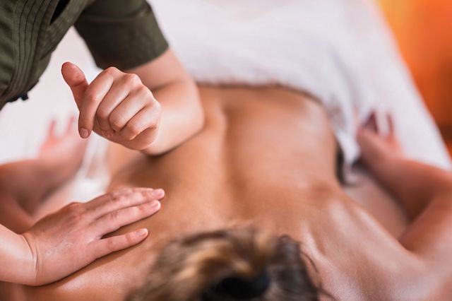 A close-up view of a person receiving a back massage at a Manhattan Chiropractic Center, focusing on their bare back with the chiropractor's hands applying pressure, indicating a therapeutic or relaxing session.