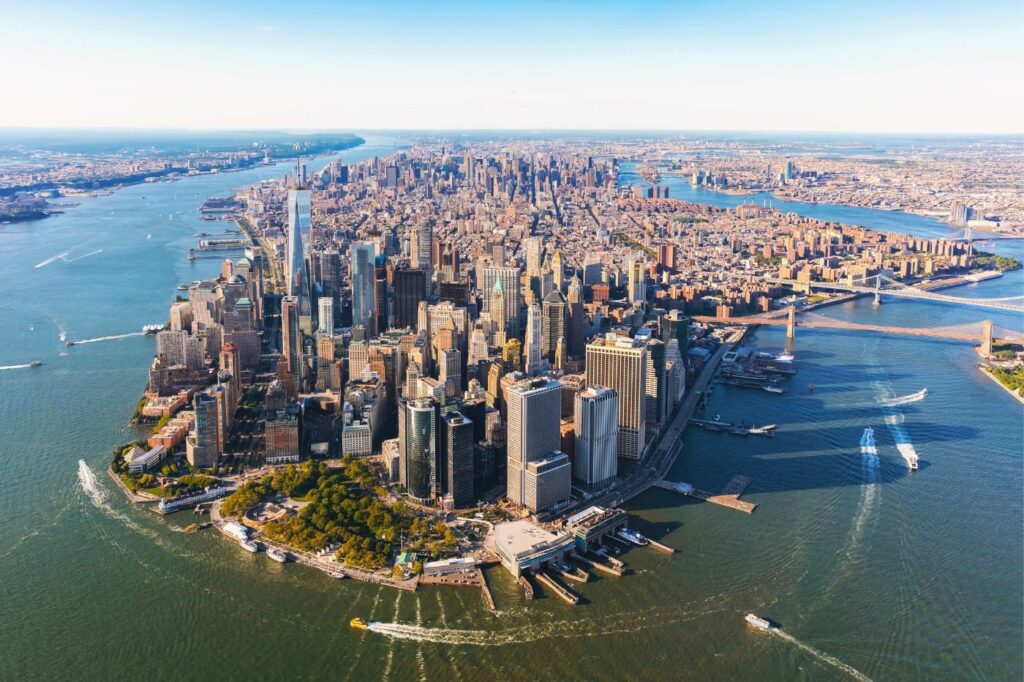 Aerial view of Lower Manhattan, showcasing the dense cluster of skyscrapers near the Lower Manhattan chiropractor, the Hudson River, and the East River under clear skies.