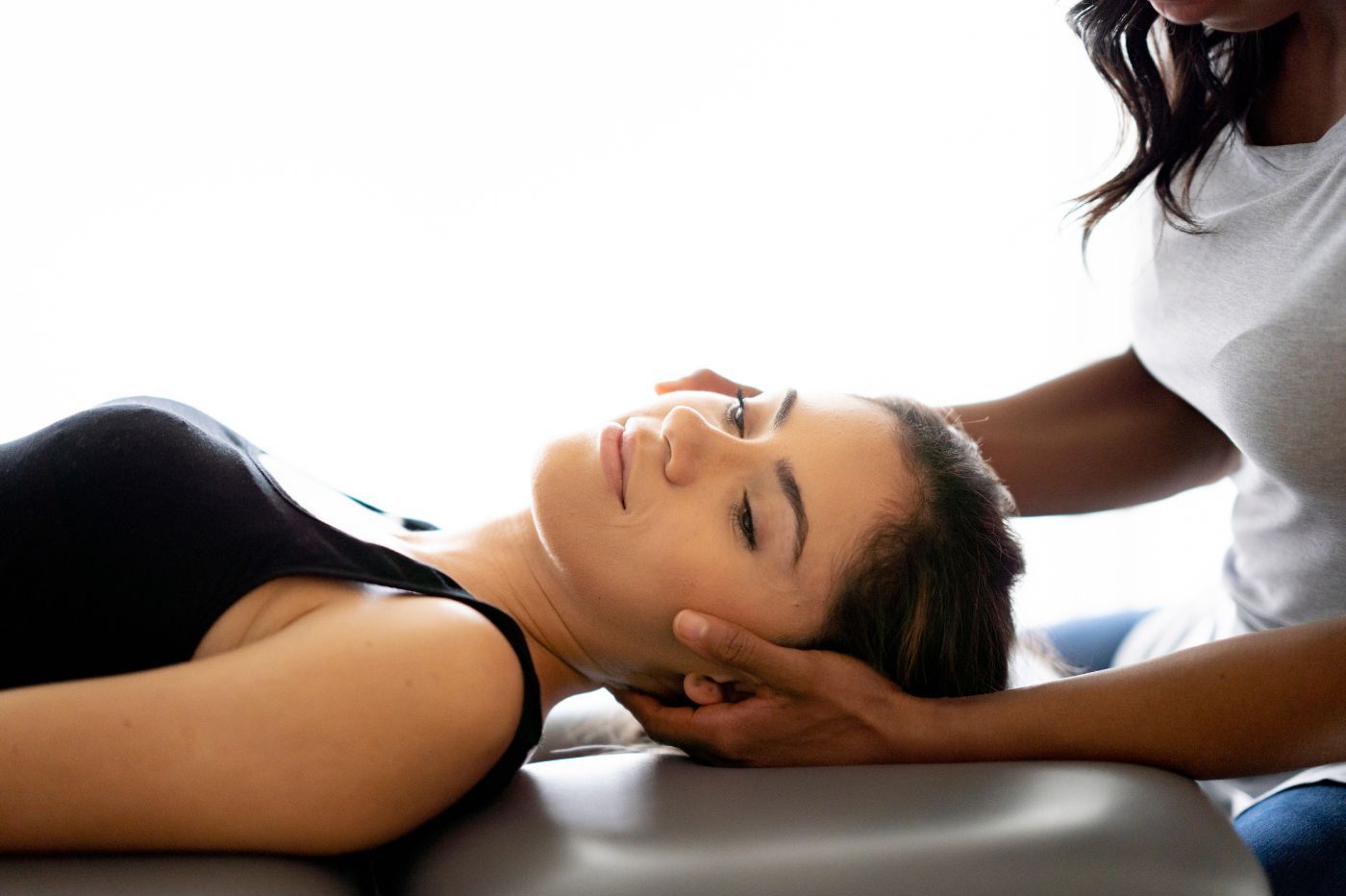 A woman receiving a gentle head massage from a therapist while lying on a massage table, conveying a sense of relaxation and care.
